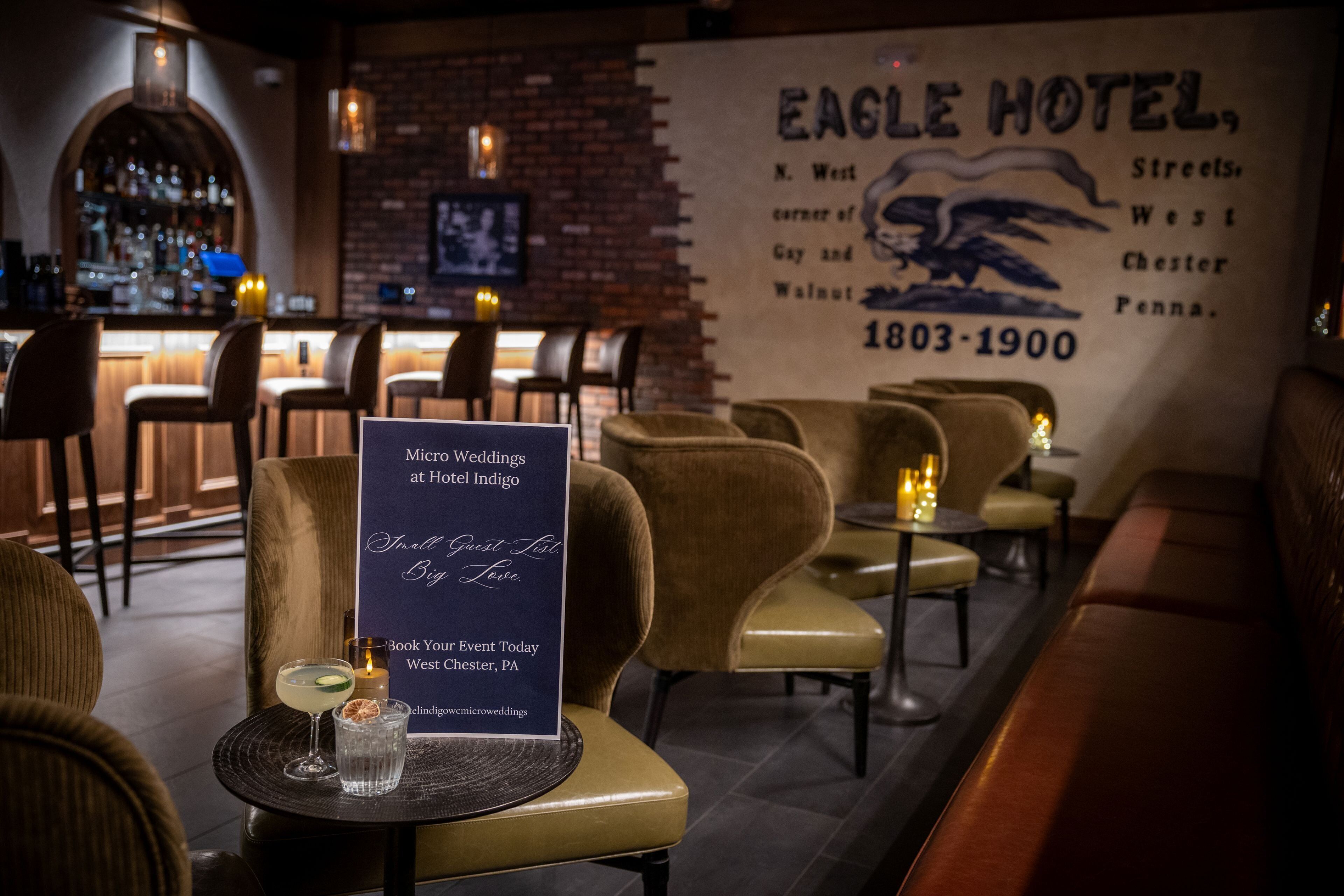 Una zona de bar con un letrero del Hotel Eagle, una pared de ladrillo y un área de estar con sillones acolchados.
