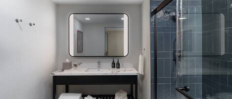 A modern bathroom with a marble sink, a large mirror, and a glass-enclosed shower.