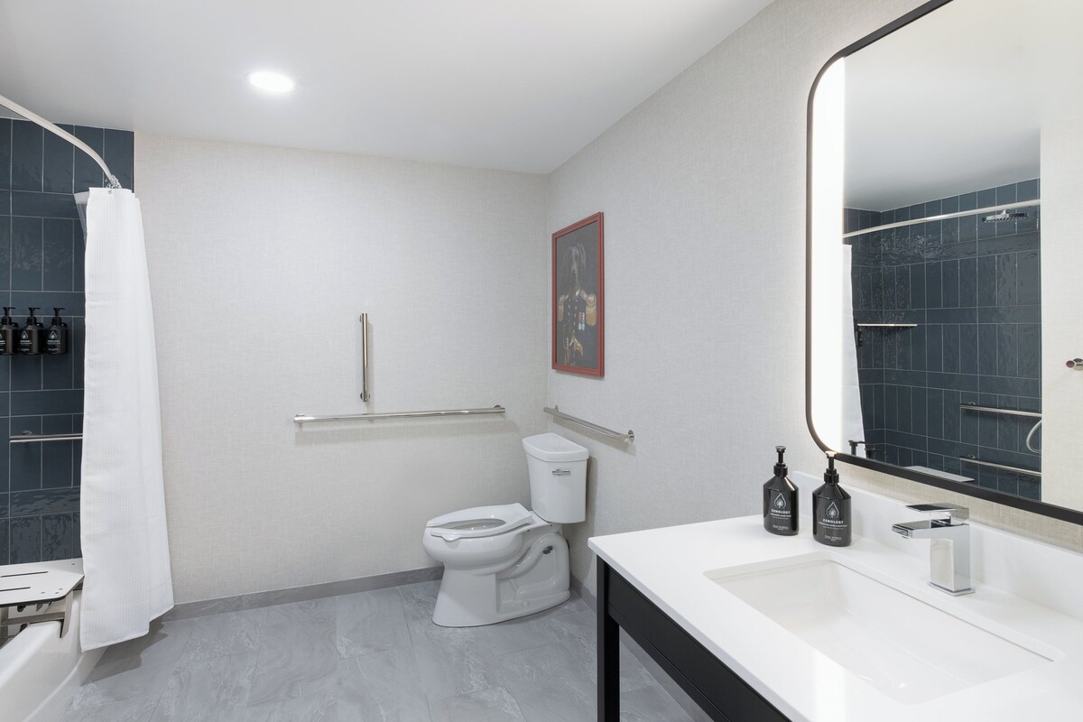 A modern bathroom with a white sink, a toilet, a shower with a white curtain, and a mirror with a black frame.