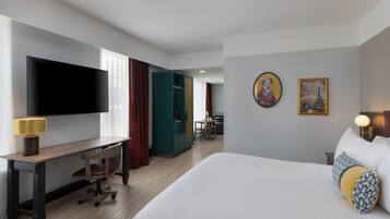 Ein Hotelzimmer mit Bett, Schreibtisch mit Stuhl, Fernseher und Essbereich im Hintergrund.