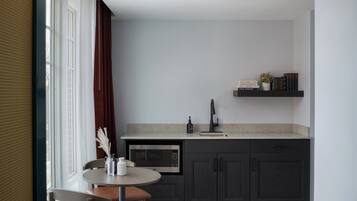 Cocina compacta con muebles oscuros, un microondas y una pequeña zona de comedor con mesa y sillas.