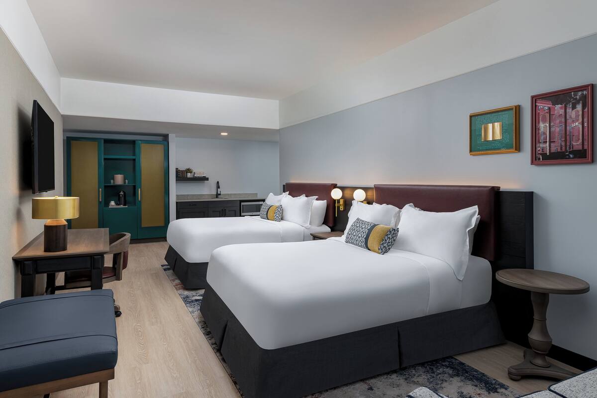 Una habitación de hotel con dos camas, un escritorio, una silla, una mesita y un televisor.