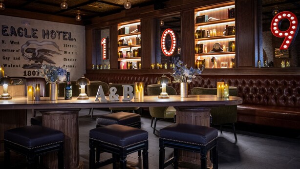 A bar area with a wooden bar, stools, and a wall with illuminated numbers. - Hotel Indigo West Chester - Downtown by IHG (West Chester)