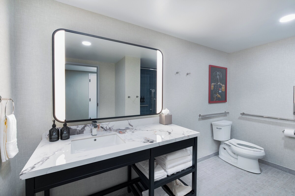 A modern bathroom with a large mirror, white marble sink, black vanity, white toilet, and a towel rack.