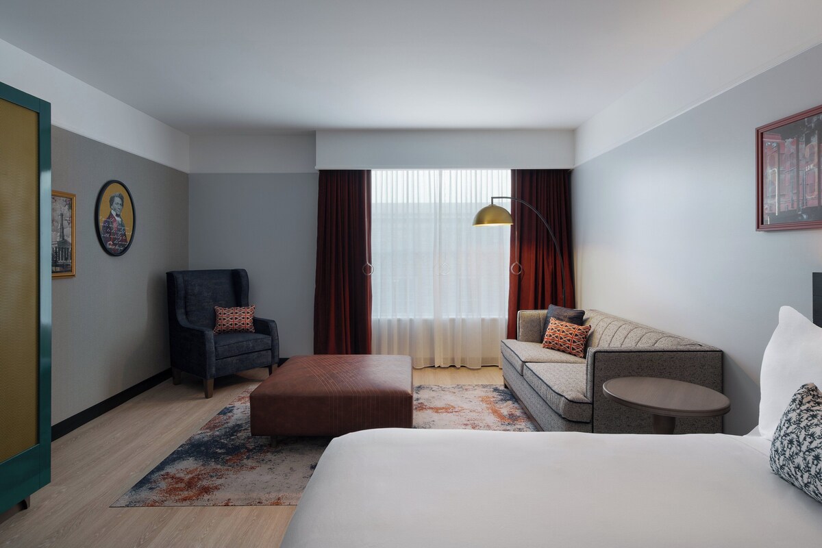 A hotel room with a bed, a sofa, a chair, a small table, and a window with curtains.