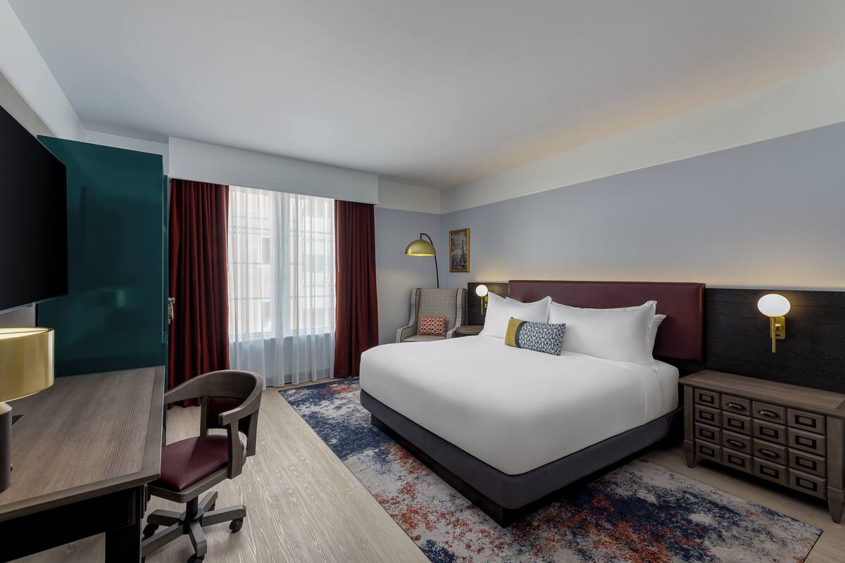 Habitación de hotel con una cama grande, un escritorio, una silla, una mesita de noche y una lámpara.