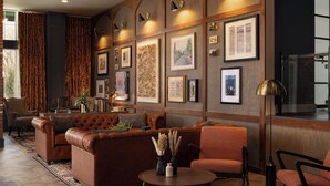 A cozy living room with a brown leather sofa, a round coffee table, and orange chairs. - Hotel Indigo West Chester - Downtown by IHG (West Chester)