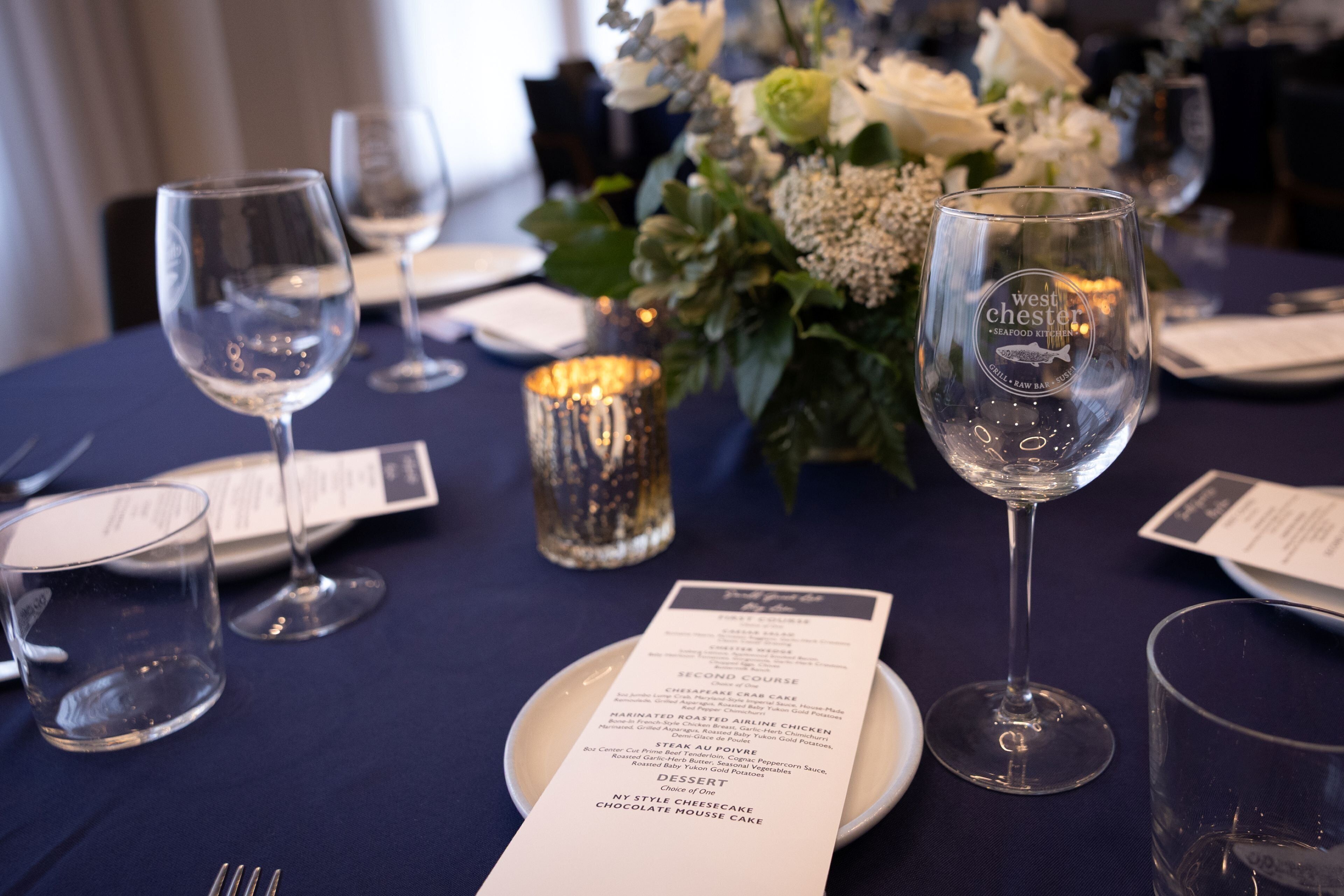 A dining table set with wine glasses, a menu, and a candle.