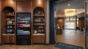 A hotel lobby with a reception desk, a large wooden display case with snacks and beverages, and a blue carpet with the hotel's name. - Hotel Indigo West Chester - Downtown by IHG (West Chester)