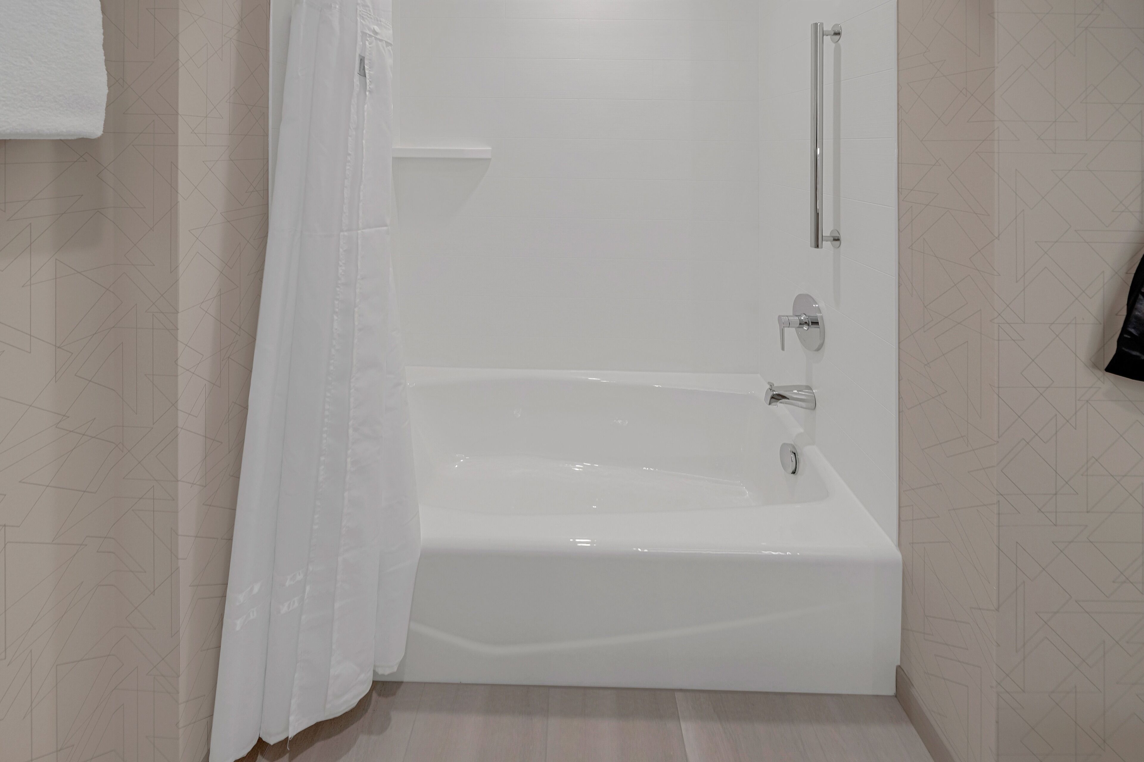 Une salle de bain moderne avec une baignoire blanche, une barre d’appui et un rideau de douche.