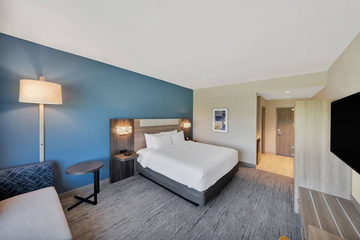 A hotel room with a large bed, a desk, a chair, a lamp, and a TV.