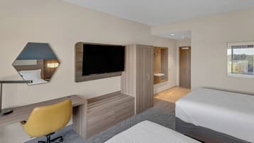 Une chambre d’hôtel comprenant un lit, un bureau avec une chaise, un téléviseur fixé au mur et une porte donnant sur une autre pièce.