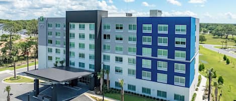 Un hotel de varios pisos con un diseño moderno, que cuenta con una zona de estacionamiento techada y espacios de estacionamiento exclusivos para vehículos eléctricos.