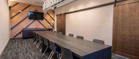A conference room with a long table, chairs, a TV screen, and a wooden wall with a geometric pattern.