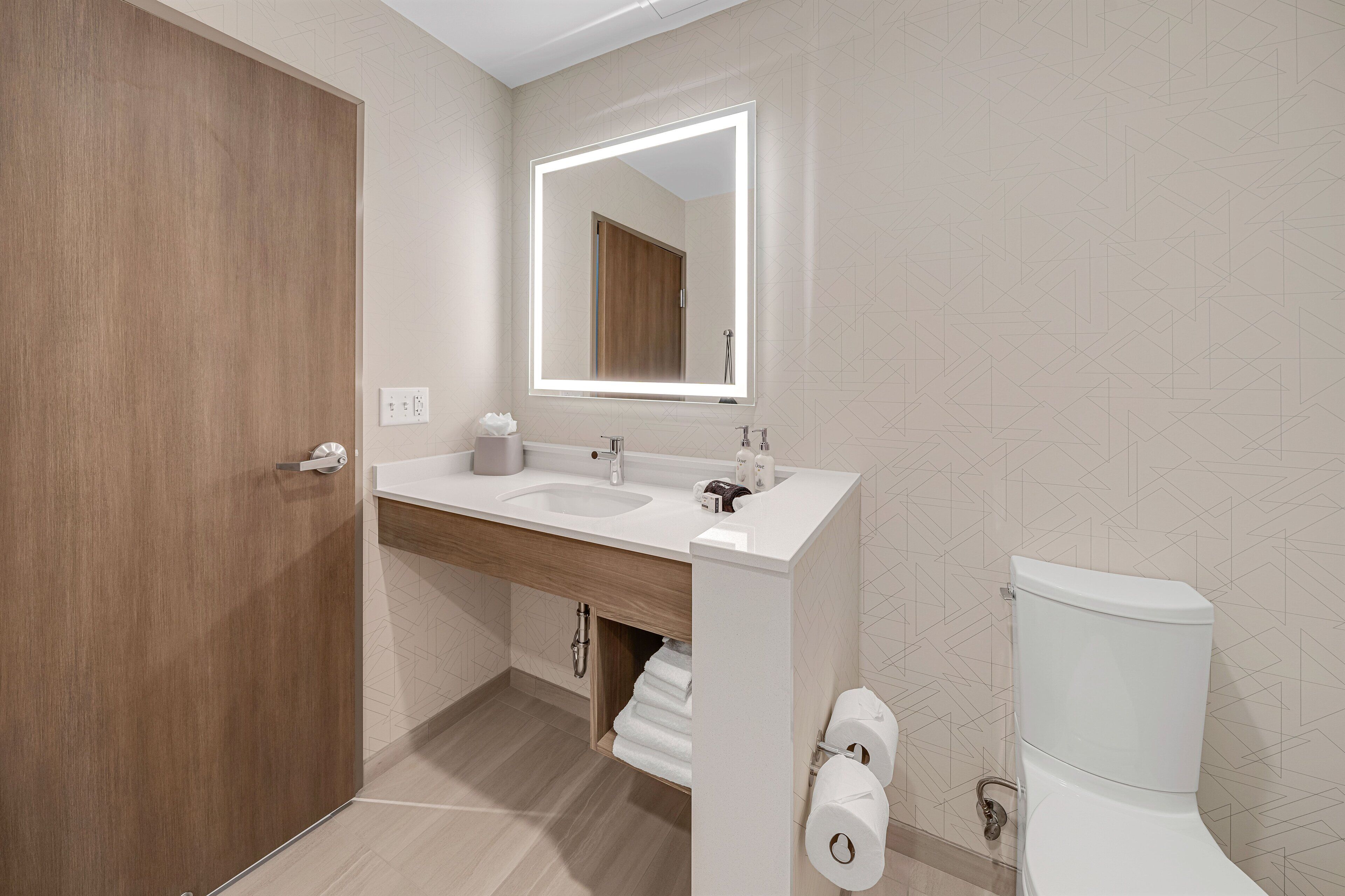 Un baño moderno con tocador de madera, un espejo grande y un inodoro.