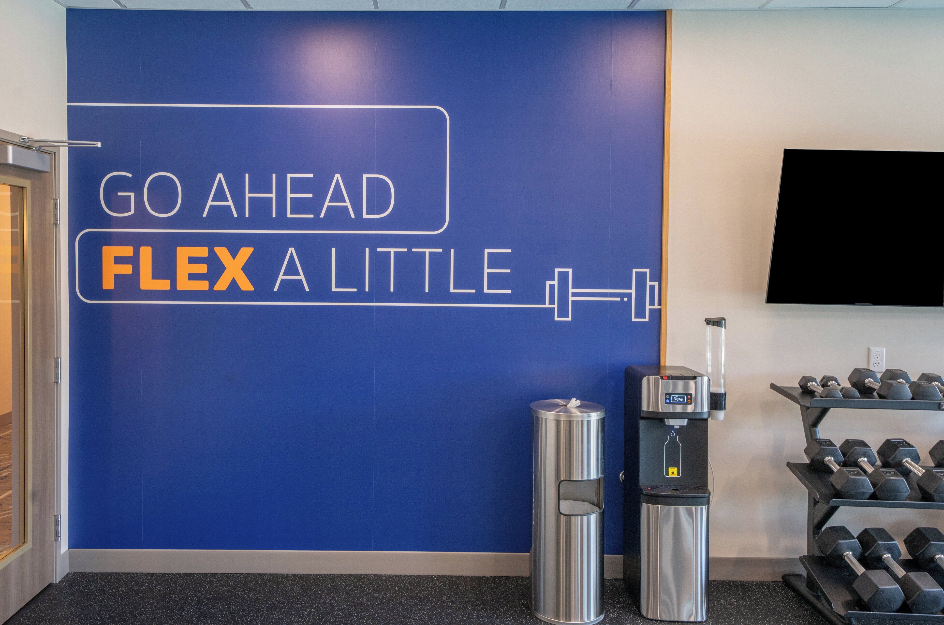 A gym with a motivational wall saying "GO AHEAD FLEX A LITTLE" and a water dispenser.