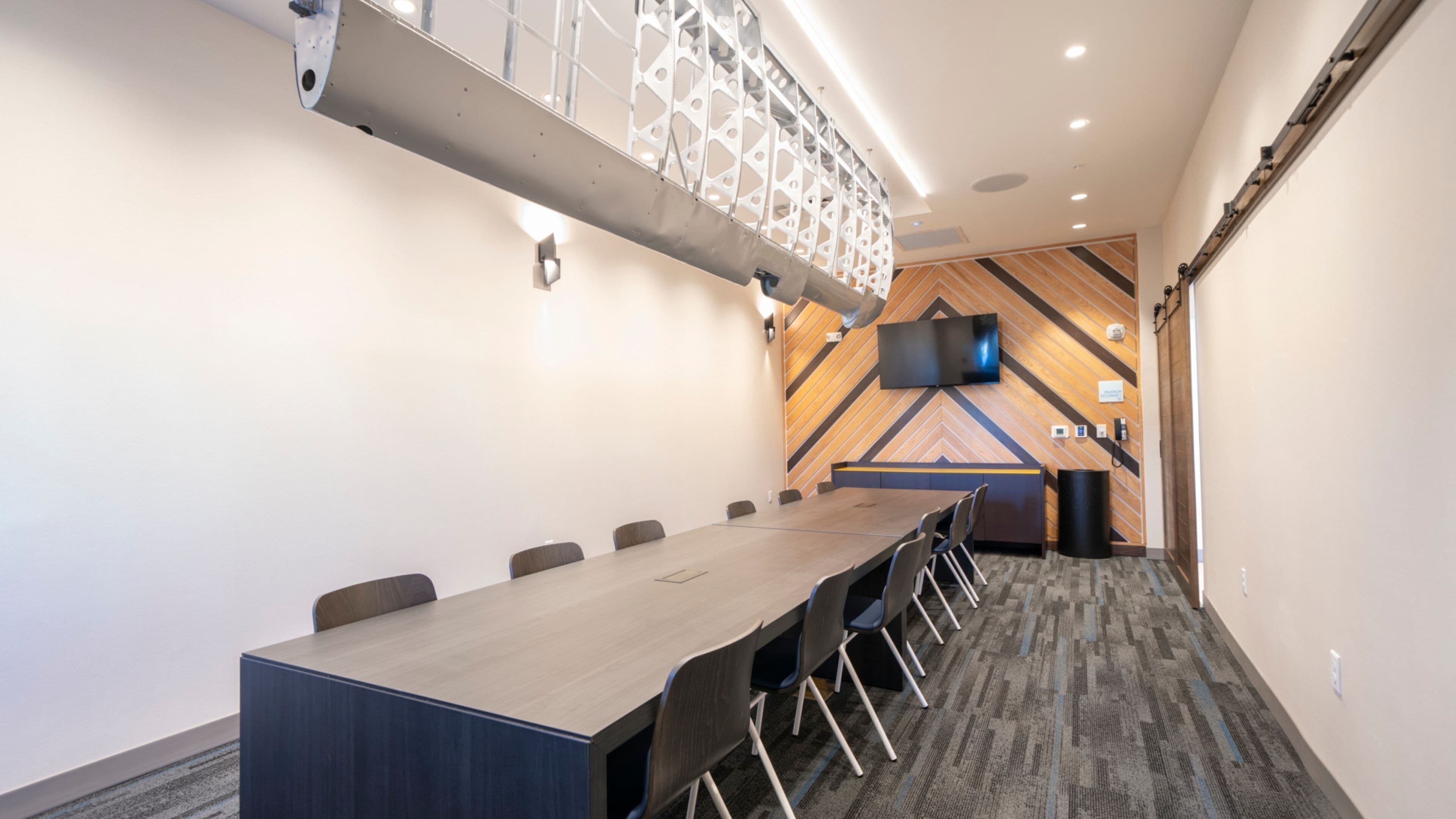 A conference room with a long table, chairs, a TV, and a patterned wall.