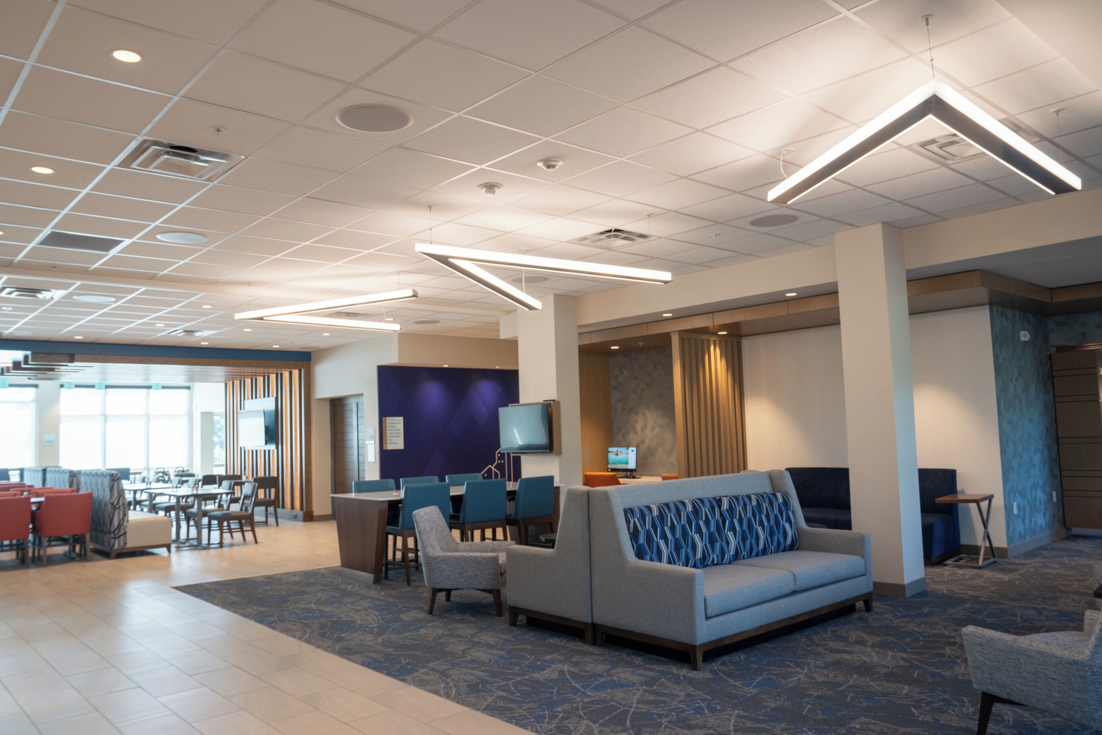 A modern hotel lobby with a seating area, a reception desk, and a dining area.
