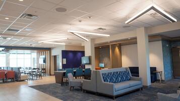 A modern hotel lobby with a seating area, a reception desk, and a dining area.