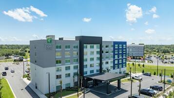Un bâtiment Holiday Inn Express & Suites au design moderne, comprenant plusieurs étages, un parking couvert et un jardin aménagé à l’avant.