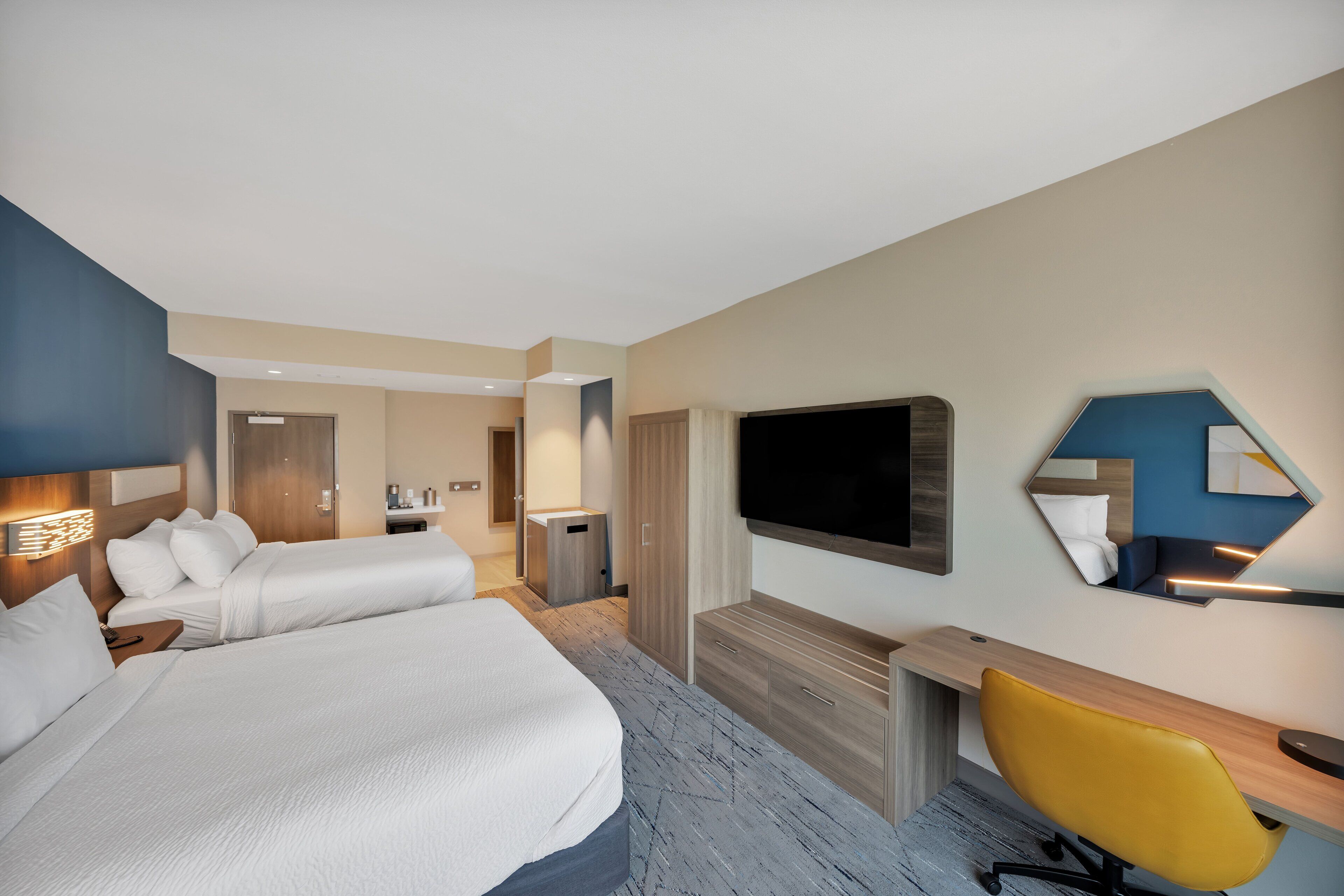 A hotel room with a large bed, a desk, a chair, a TV, and a mirror.