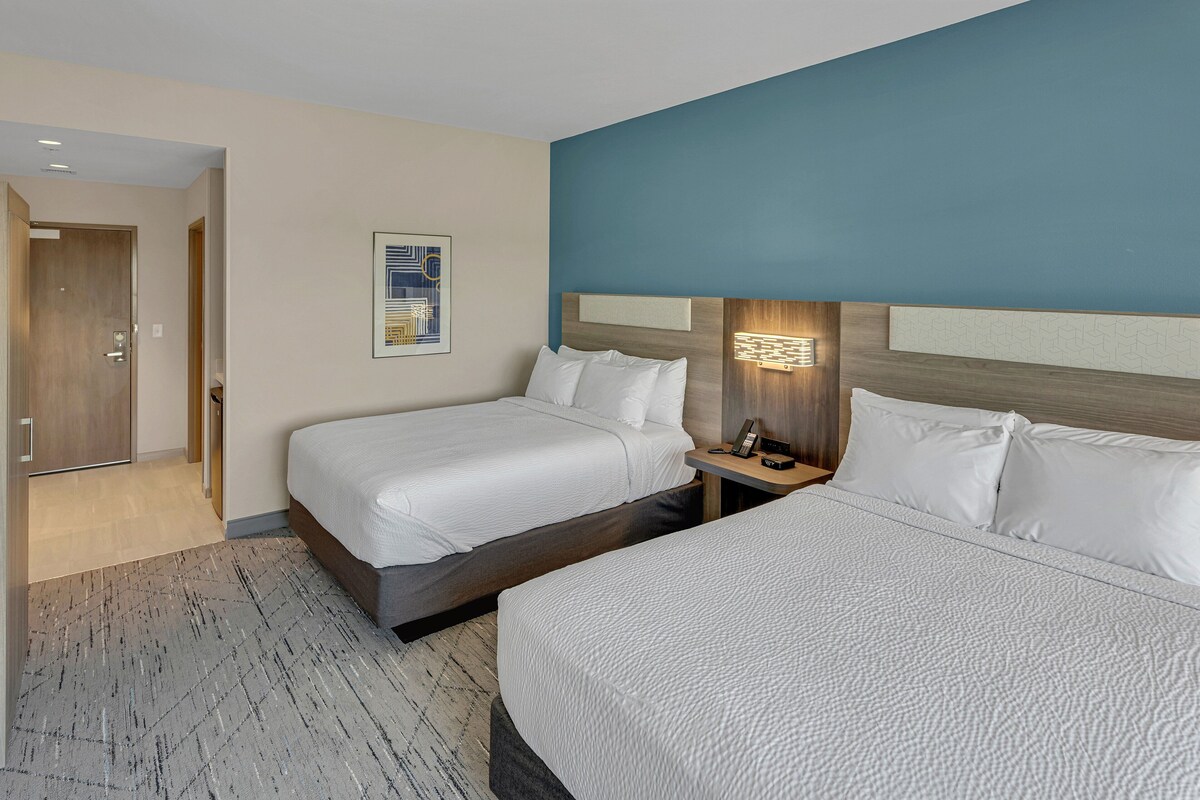 Une chambre d’hôtel avec deux lits, une table de chevet, une lampe fixée au mur et une porte donnant sur une autre pièce.