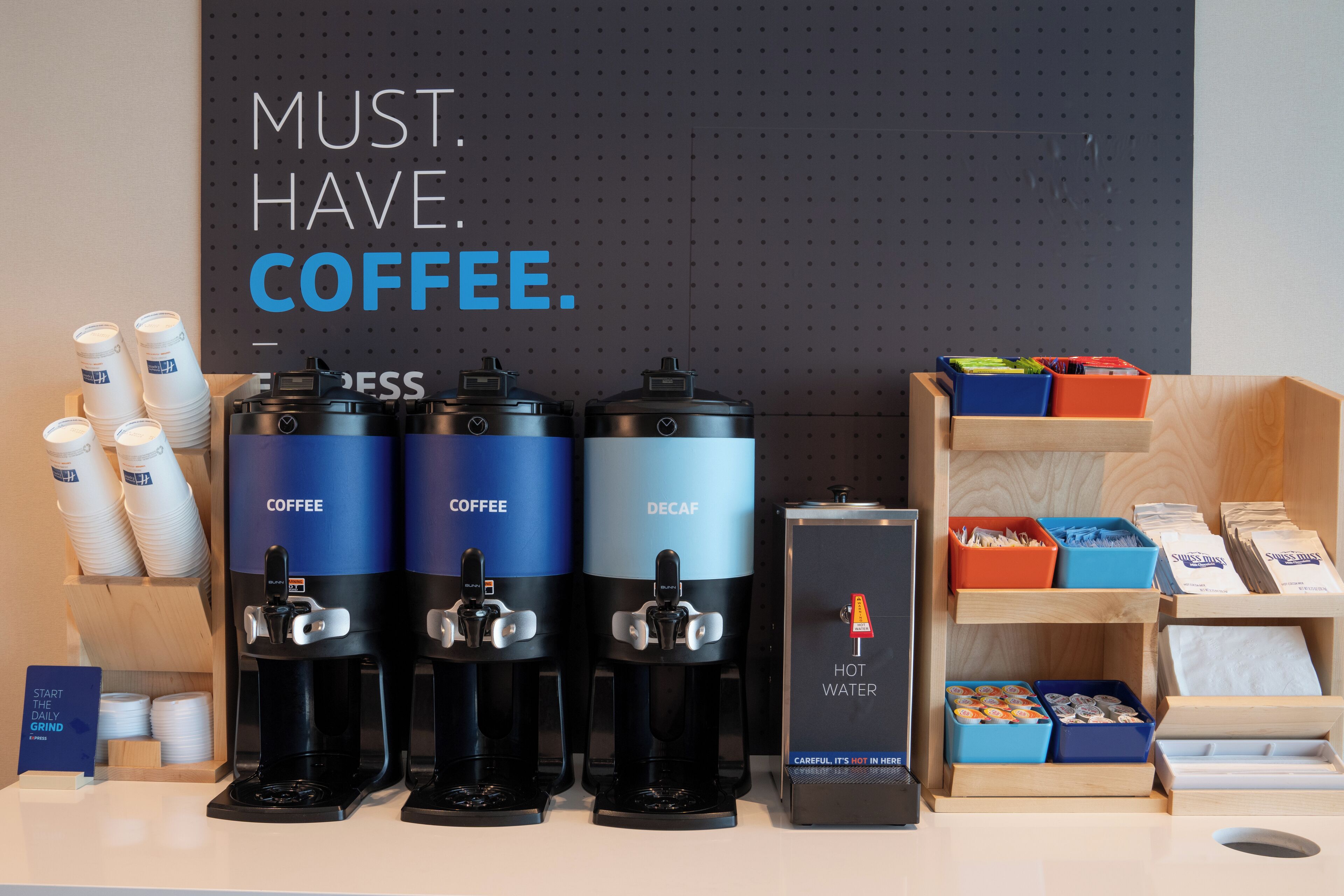 Un espace dédié au café, équipé de trois distributeurs de café, d’un distributeur d’eau et d’un panneau indiquant : « IL FAUT ABSOLUMENT DU CAFÉ ».