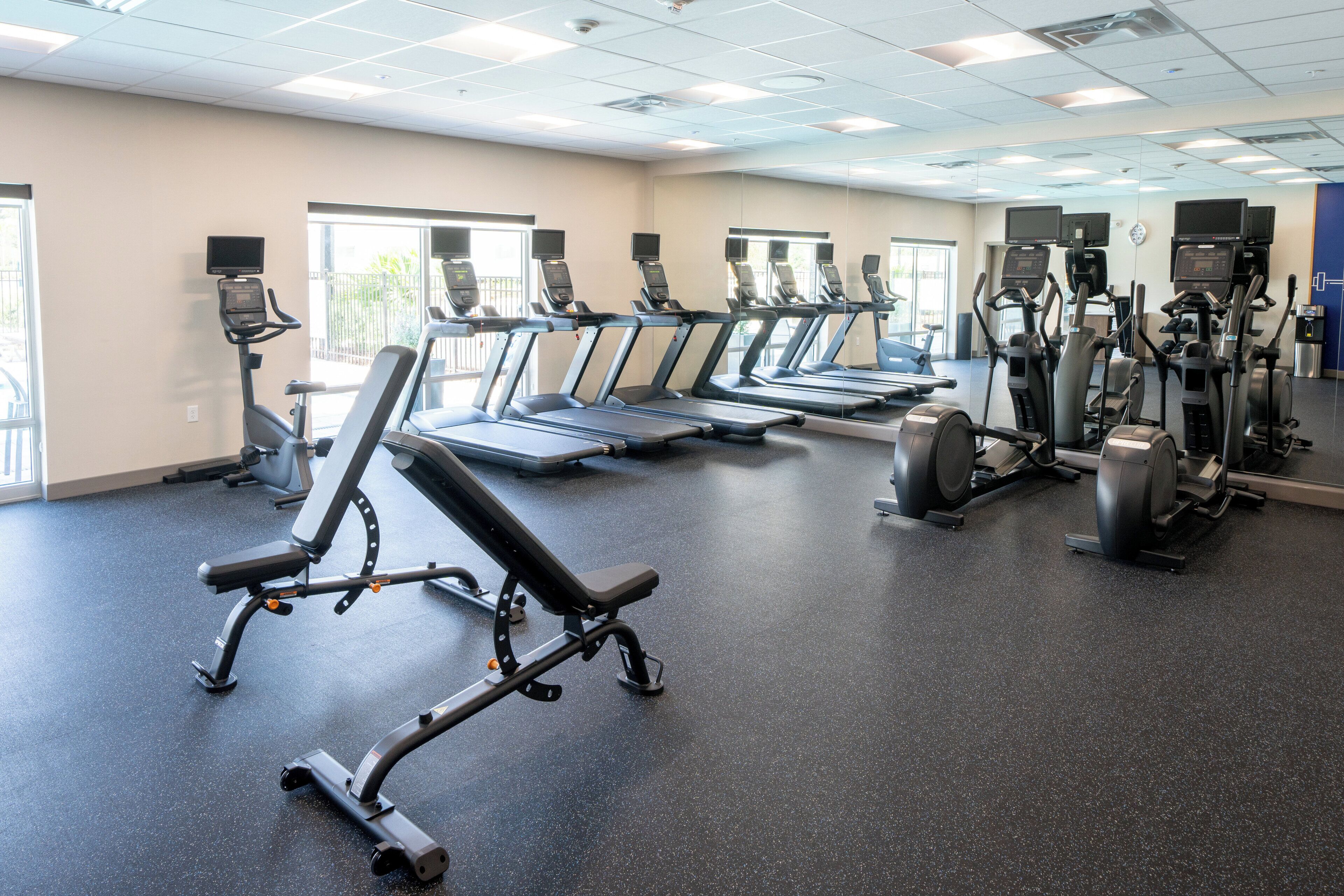 A gym with multiple treadmills, elliptical machines, and weight benches.