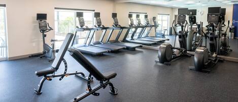 A gym with multiple treadmills, elliptical machines, and weight benches.