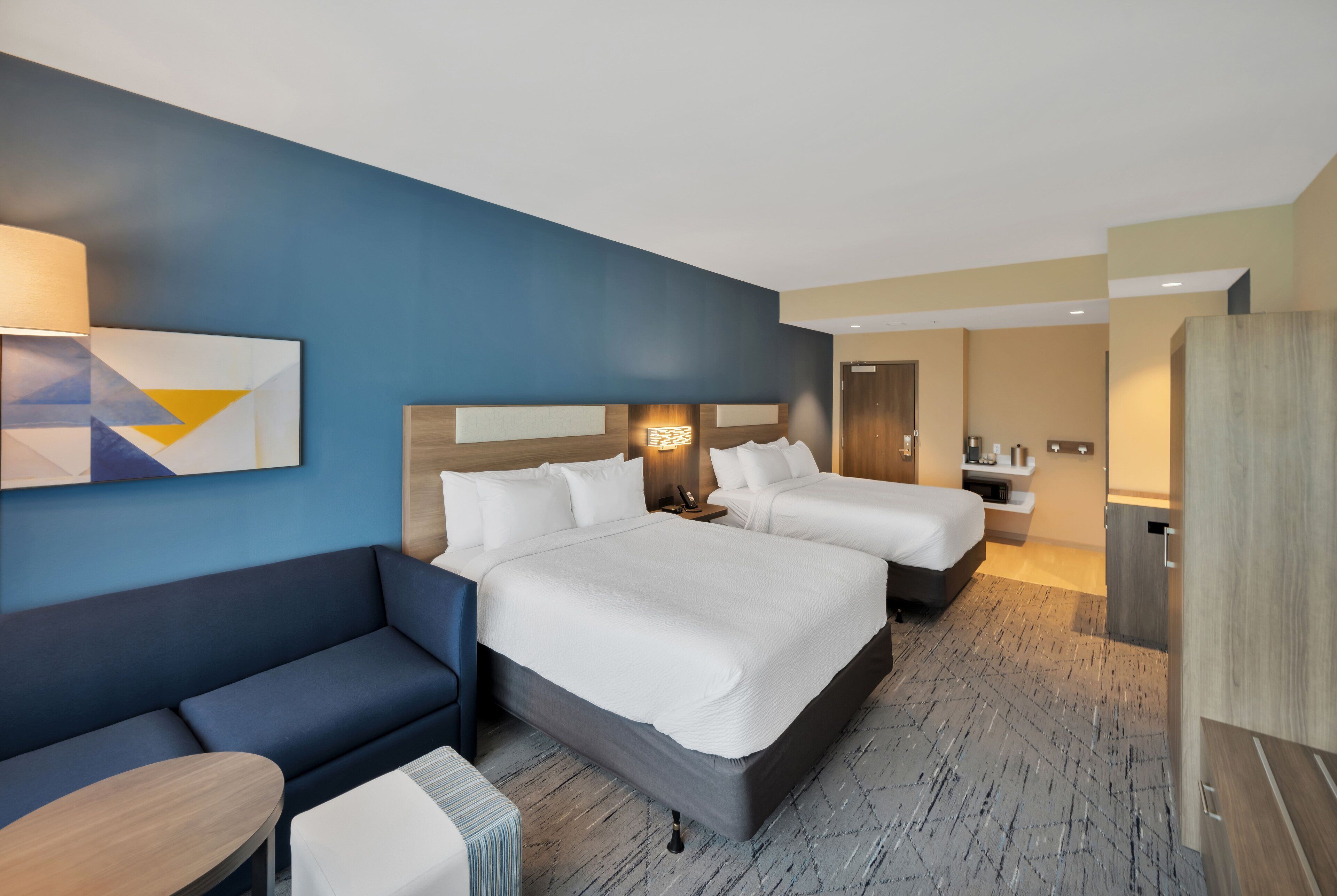 A hotel room with a large bed, a sofa, a desk, and a bathroom.