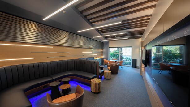 A modern lounge area with a curved black sofa, wooden ottomans, and a coffee table. - Holiday Inn Express & Suites Fort Walton Beach Eglin Area by IHG (Fort Walton Beach)