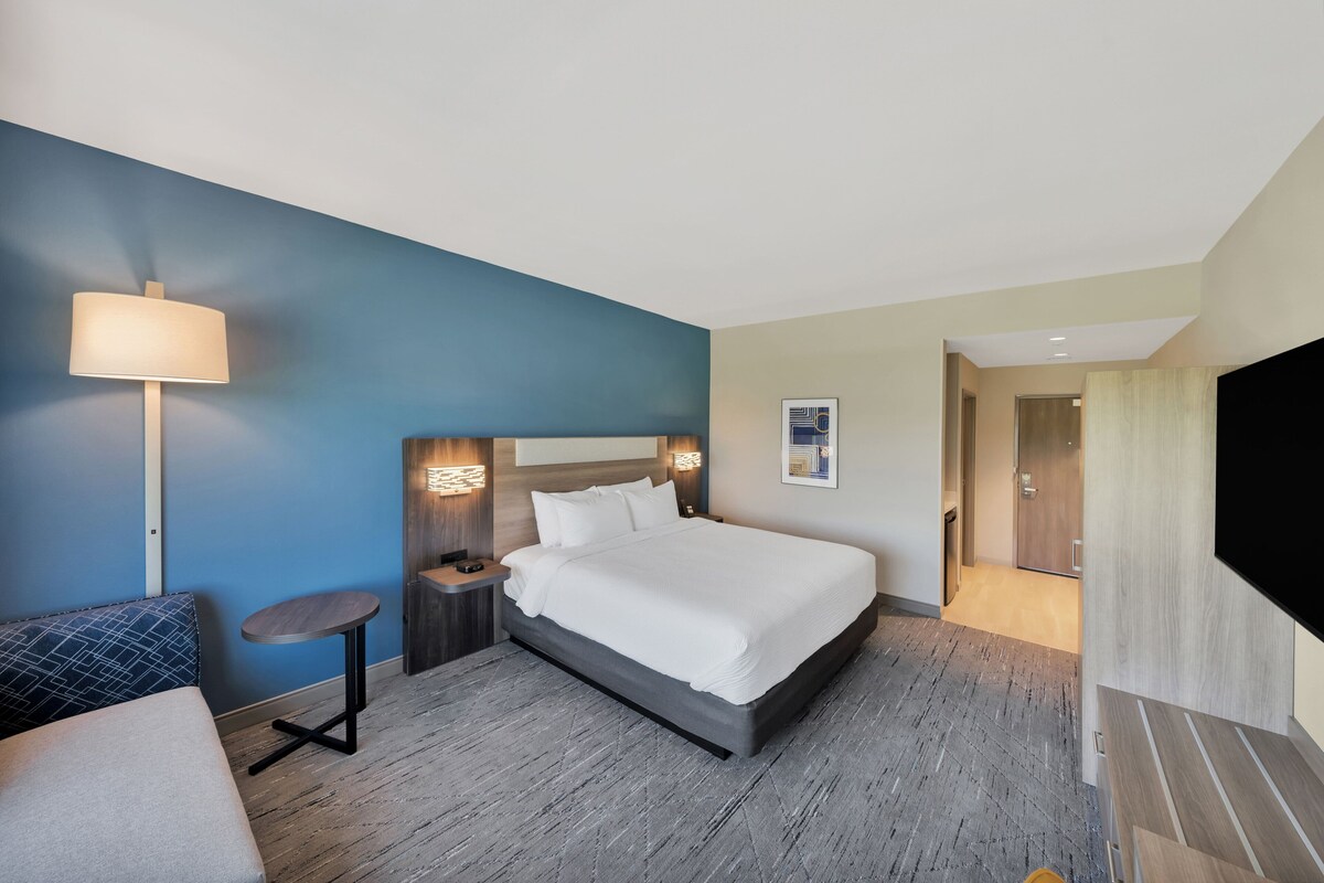 Une chambre d’hôtel avec un grand lit, un bureau, une chaise, une lampe et un téléviseur.