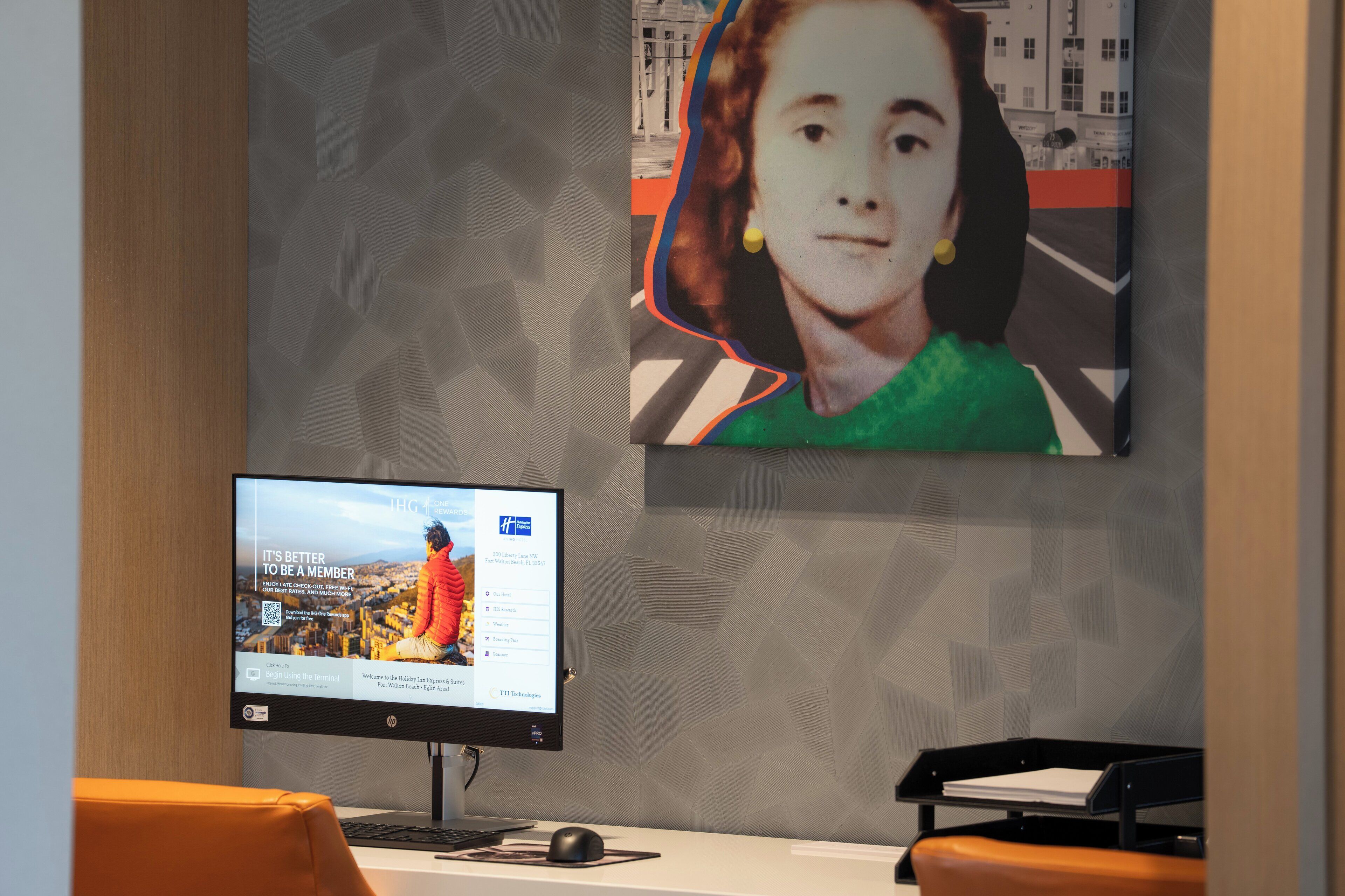 A reception area with a computer monitor displaying a webpage, a framed picture on the wall, and a desk with a chair.