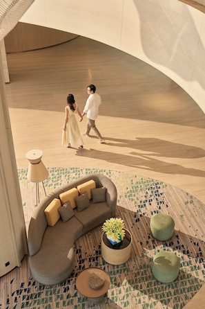 A modern interior with a curved wooden ceiling, a sectional sofa with cushions, a small round table, and a potted plant. - Holiday Inn & Suites Vientiane by IHG (Vientiane)
