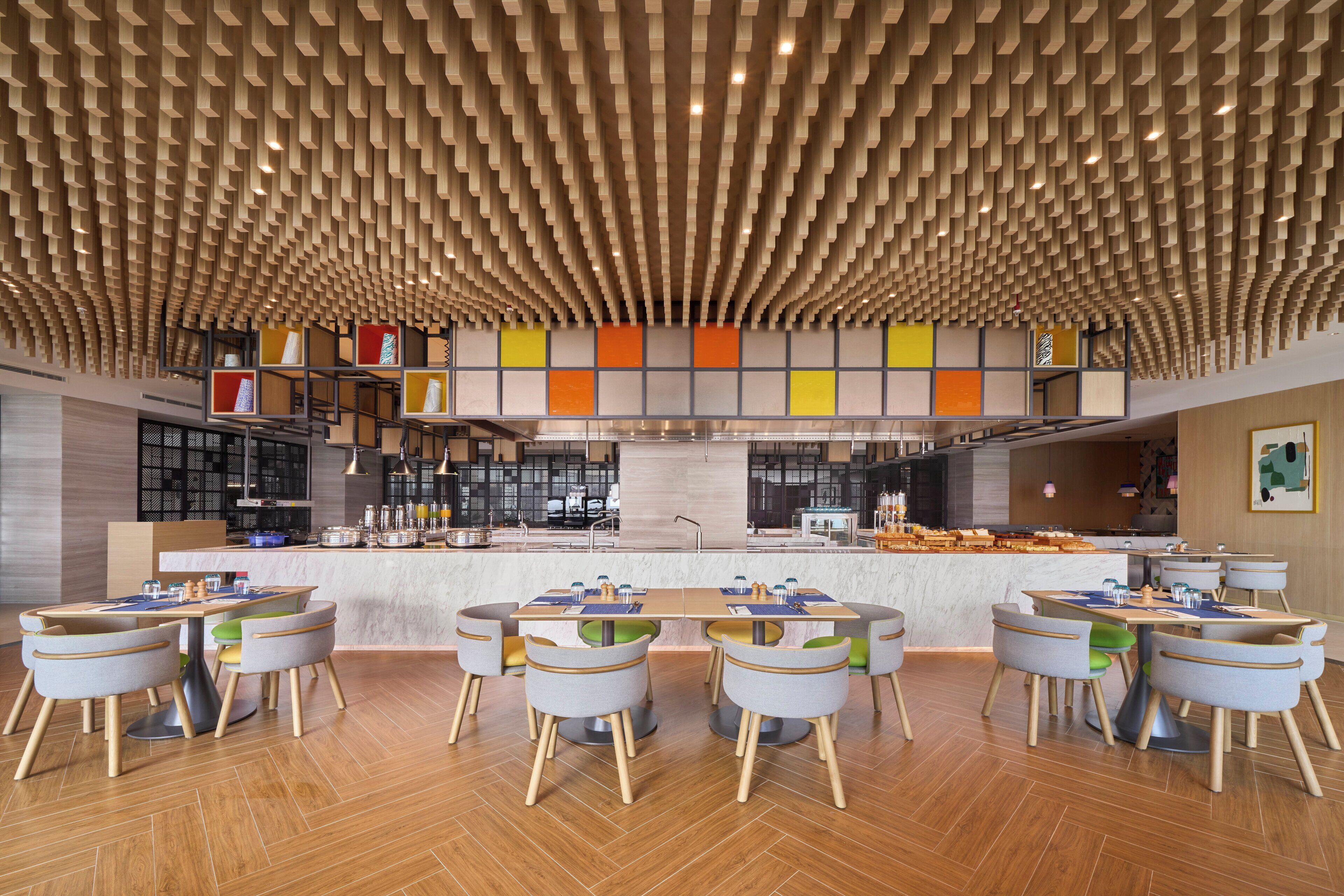 Een modern restaurant met een opvallend plafondontwerp, een centraal gelegen bar en een zithoek met ronde tafels en stoelen.