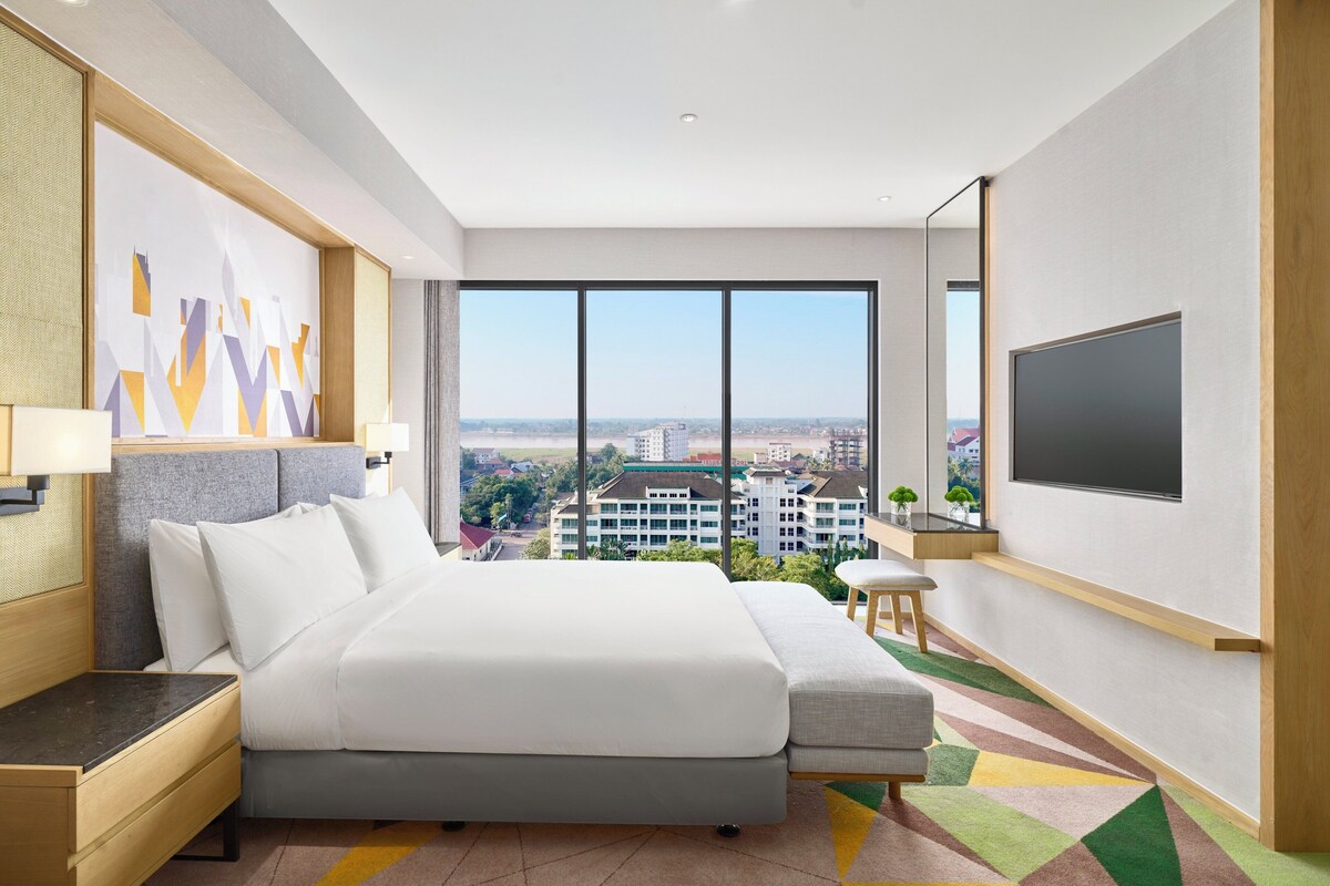 Una habitación de hotel moderna con una cama grande, televisión y vistas a la ciudad.