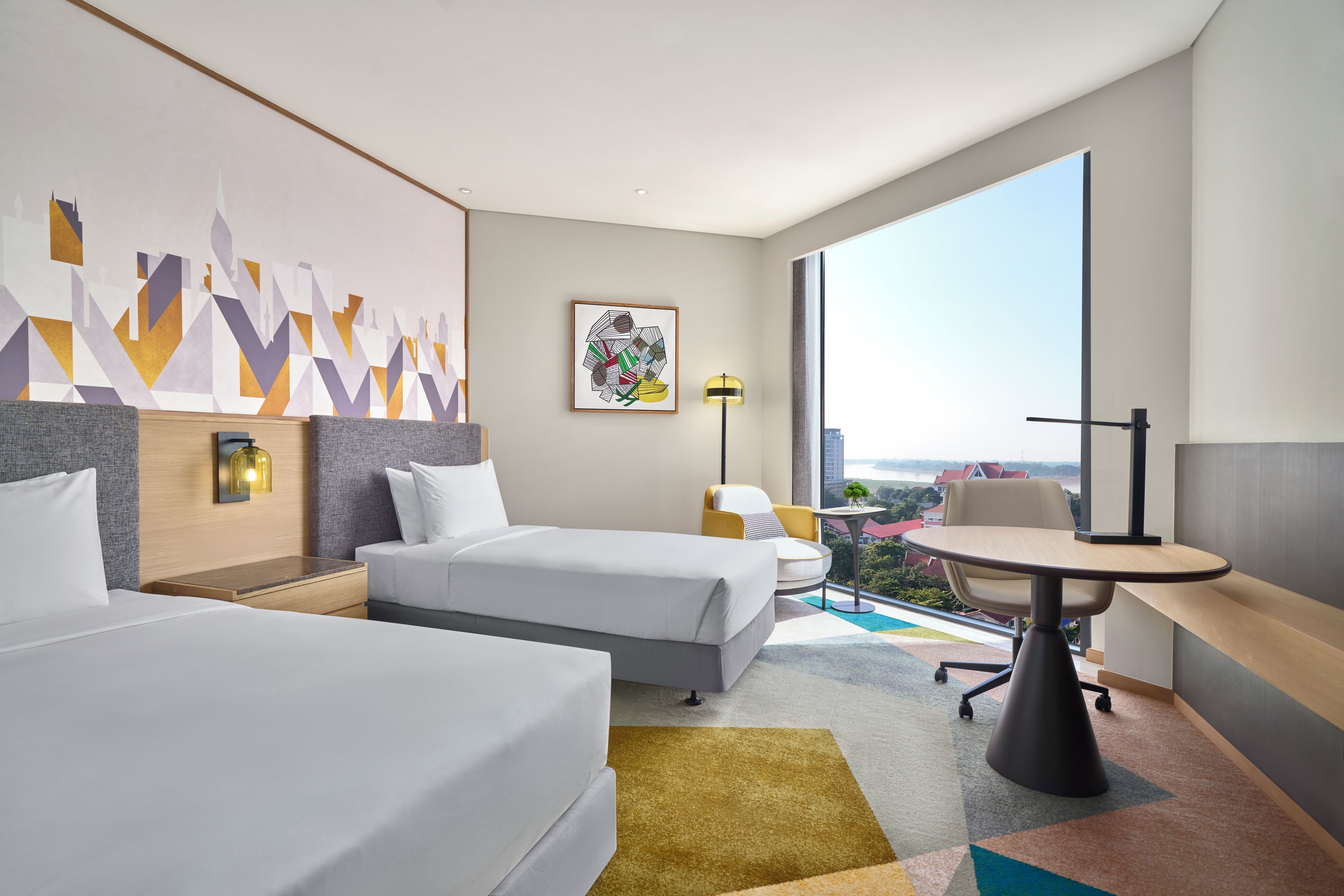 A modern hotel room with two beds, a desk, and a large window offering a city view.