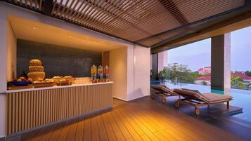 A modern outdoor area with a wooden reception desk, a fruit bowl, and a poolside lounge with sun loungers.