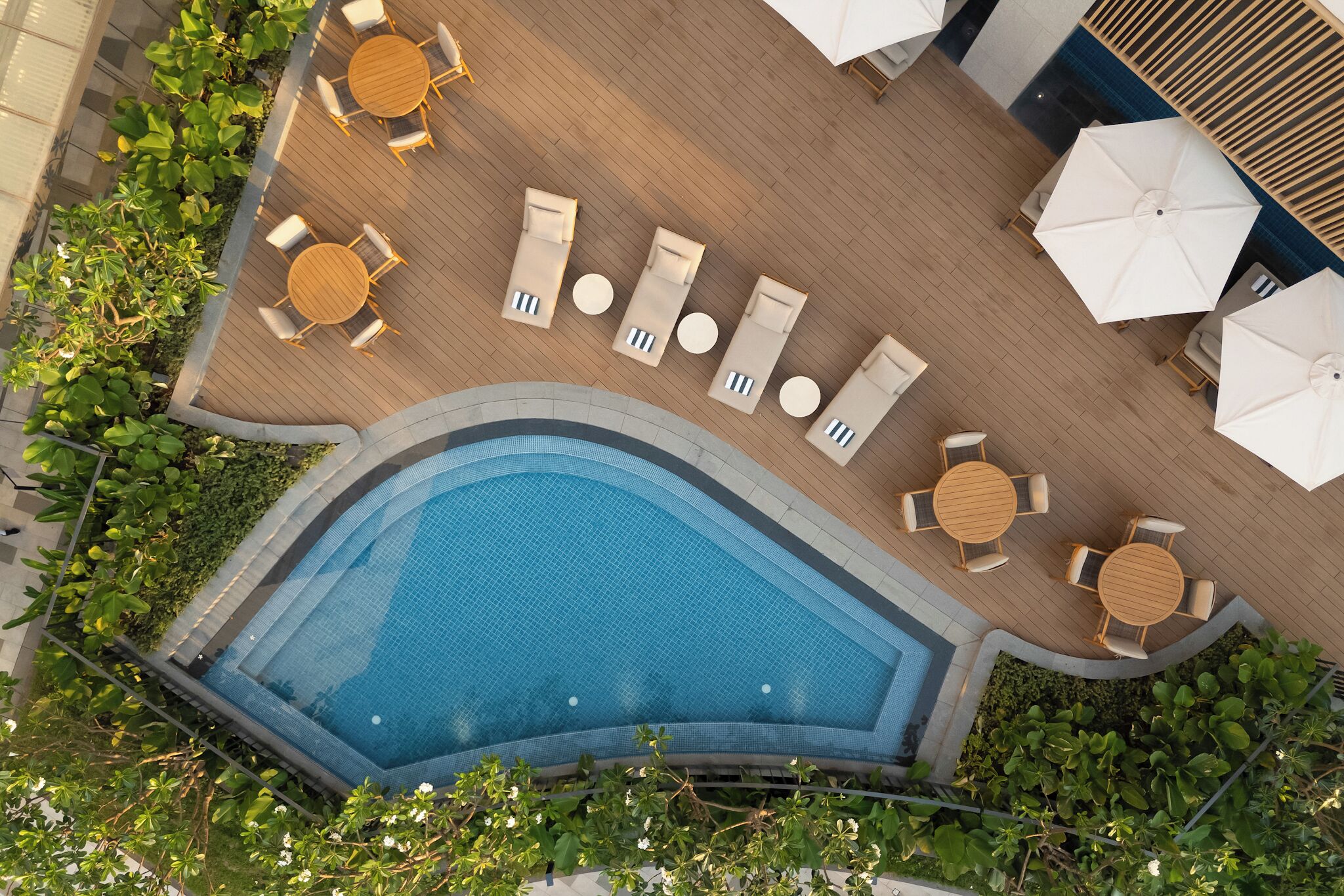 Vista aérea de una zona de piscina con sillones de descanso, sombrillas y una terraza de madera.