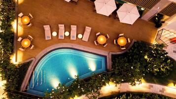 An aerial view of a rooftop pool area with sun loungers, umbrellas, and a swimming pool surrounded by greenery.