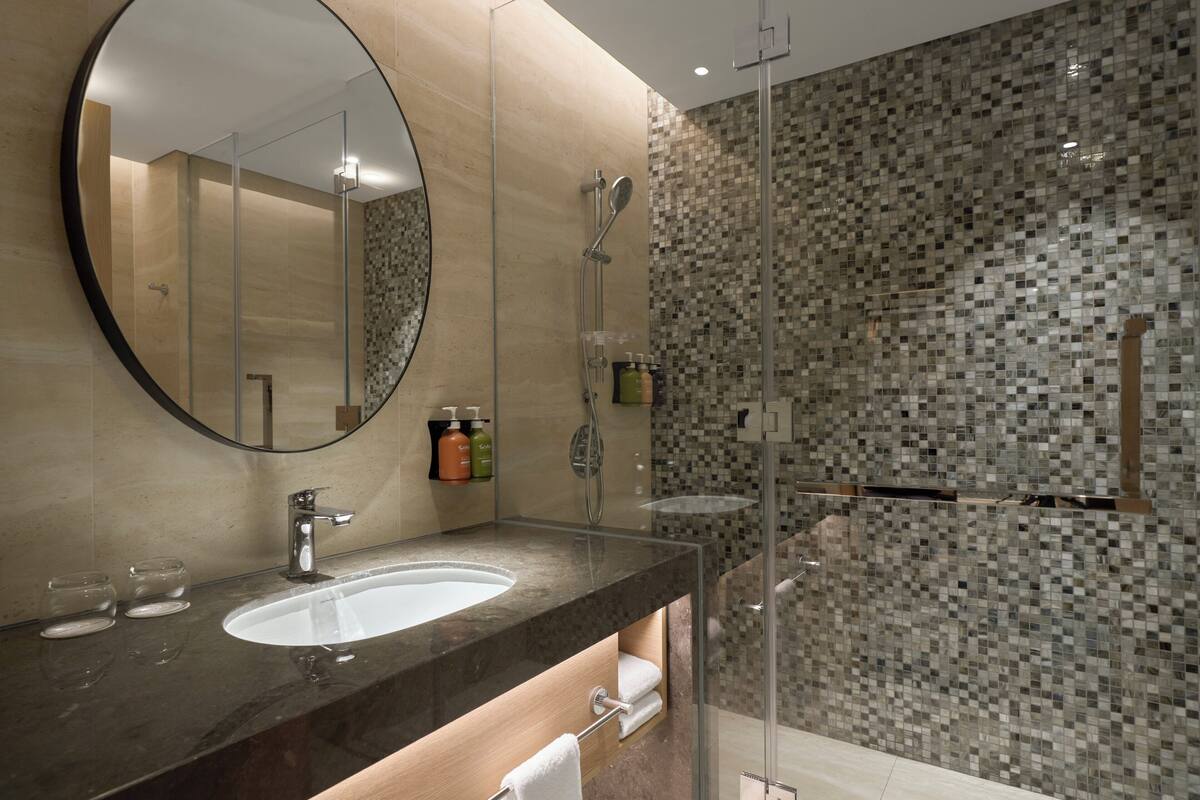 A modern bathroom with a large mirror, a sink, and a shower area.