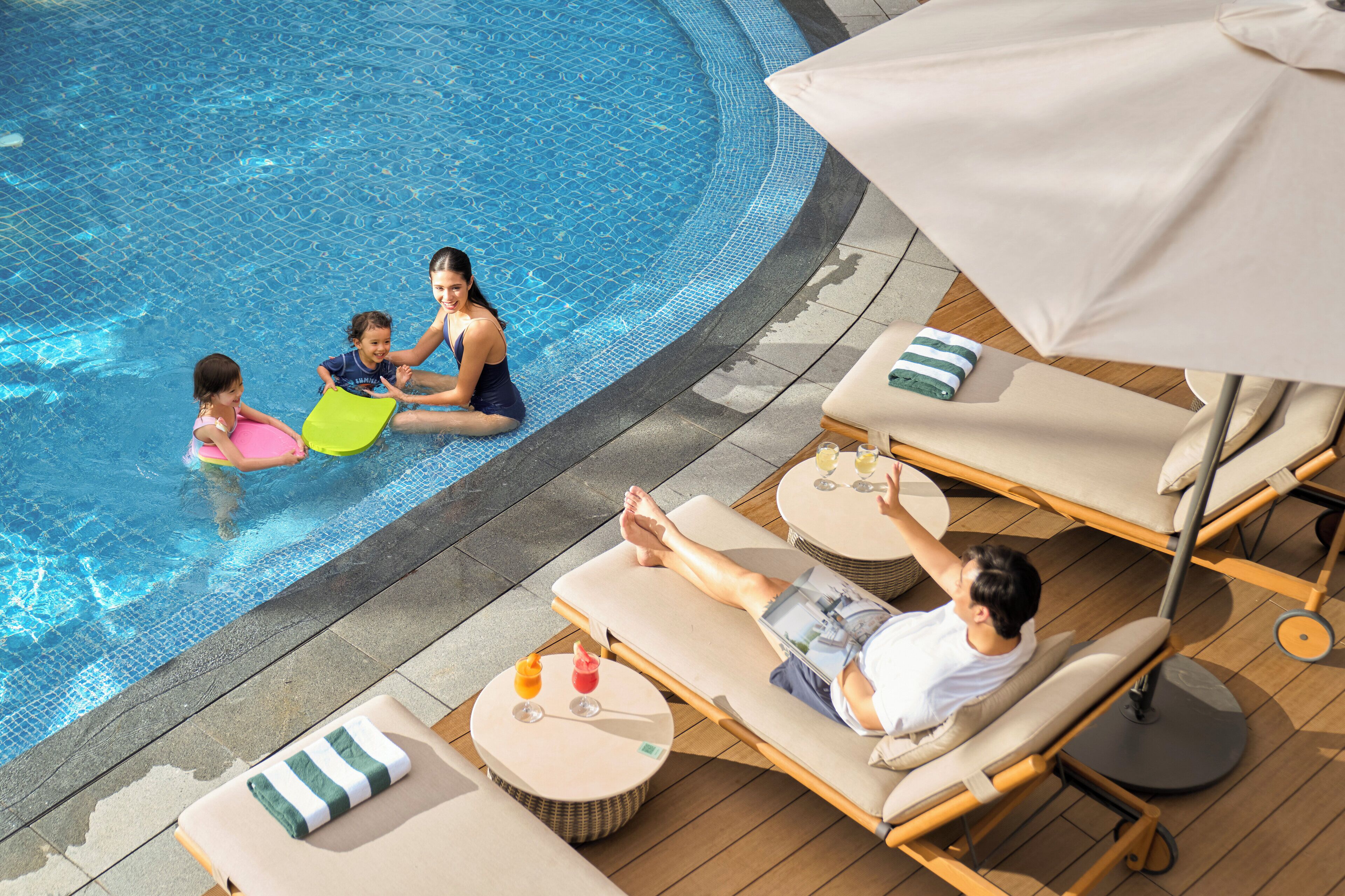 Un área junto a la piscina con sillones de descanso, una mesa con bebidas y una persona relajándose.