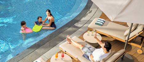 Un área junto a la piscina con sillones de descanso, una mesa con bebidas y una persona relajándose.