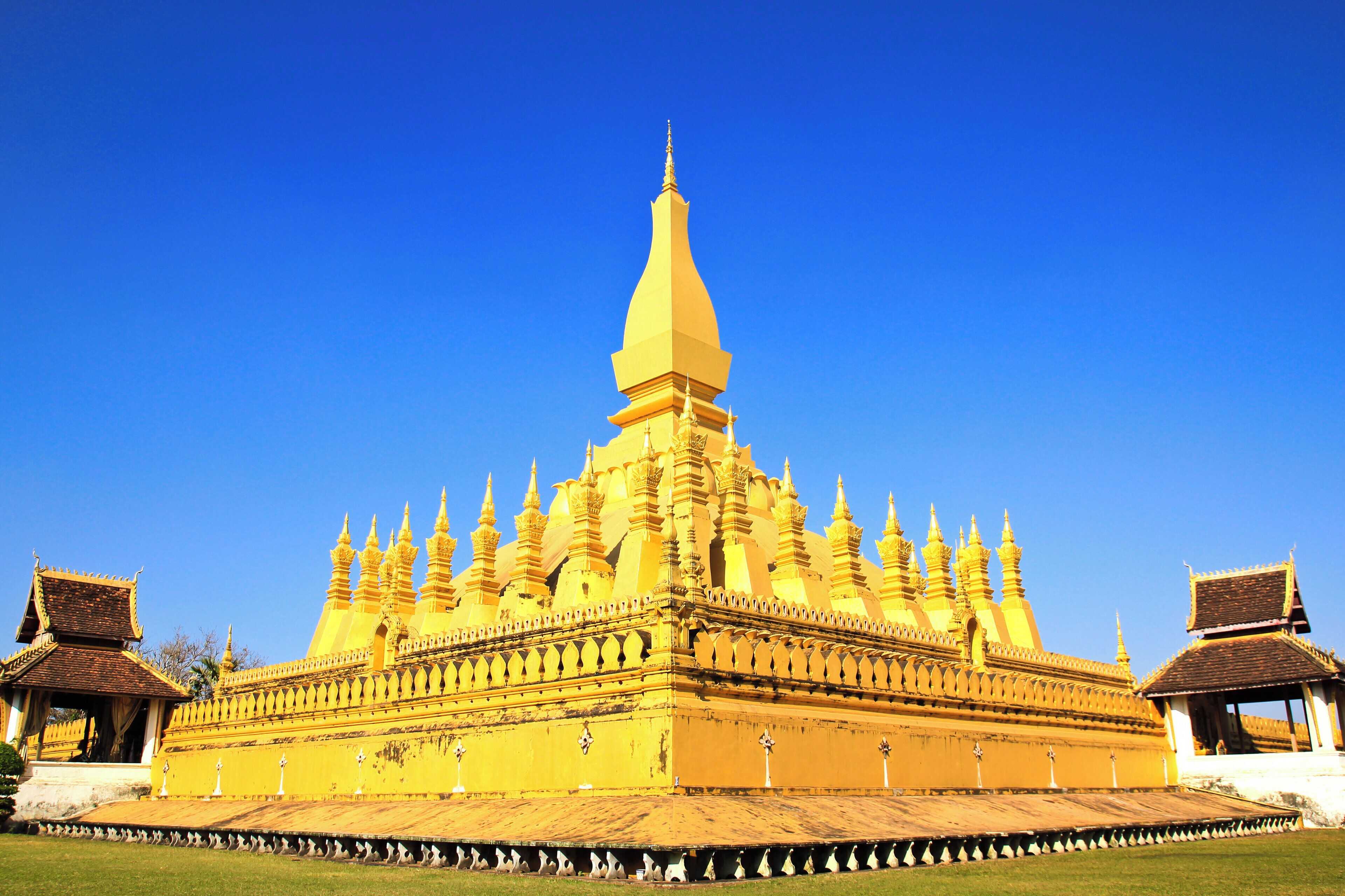 A large, golden temple with multiple spires and a central tower, surrounded by a well-maintained lawn.