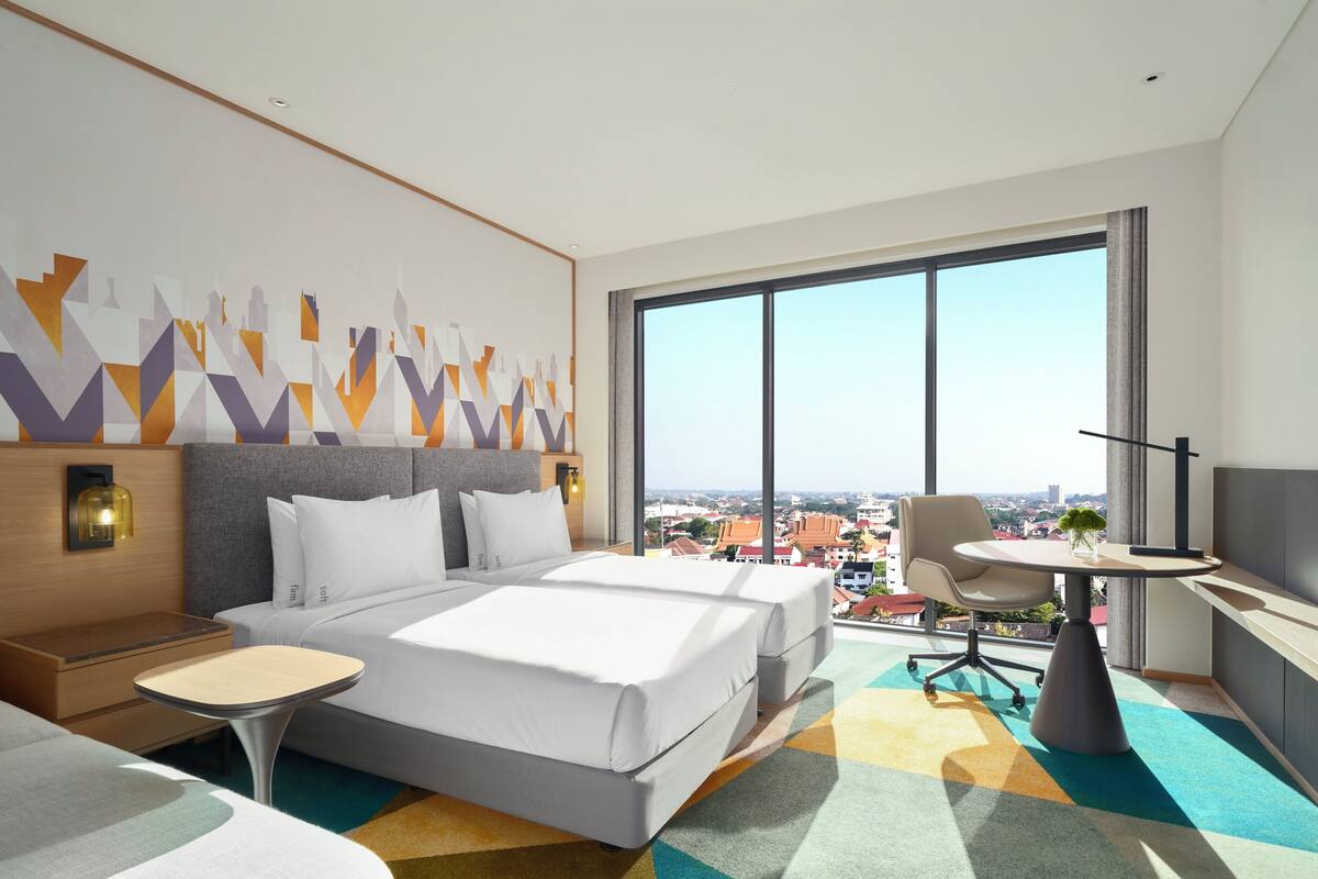A modern hotel room with a large bed, a desk, and a view of the city.