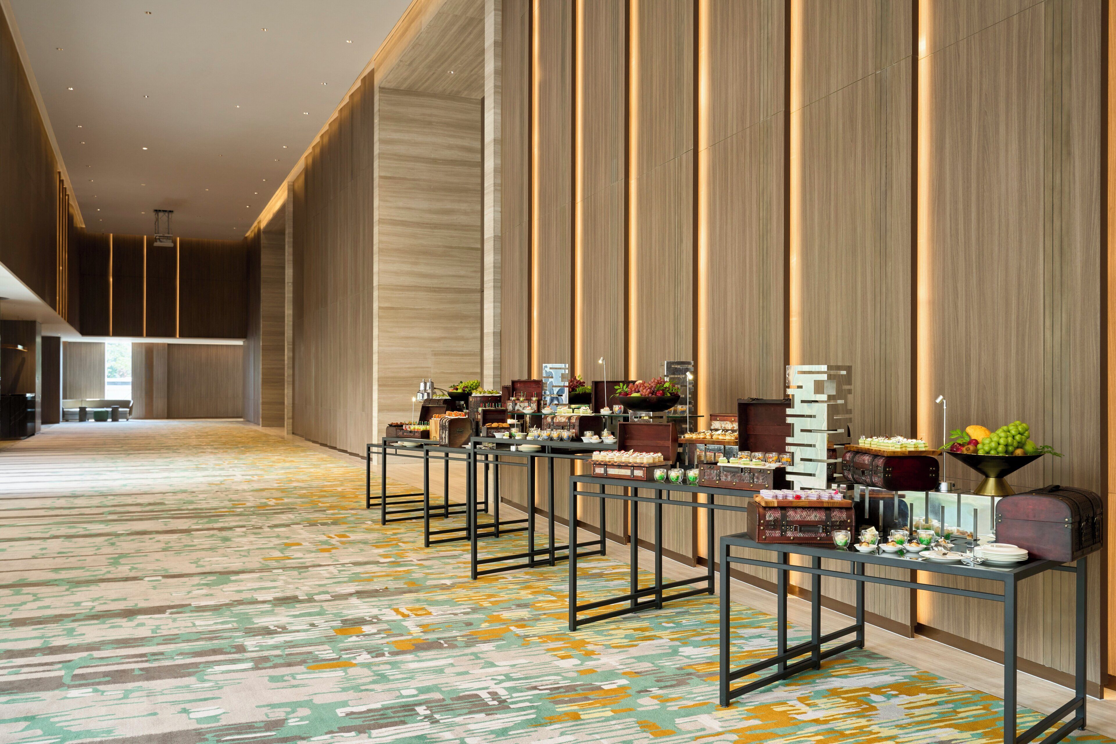 A spacious hotel lobby with a long reception desk, a patterned carpet, and a modern interior design.