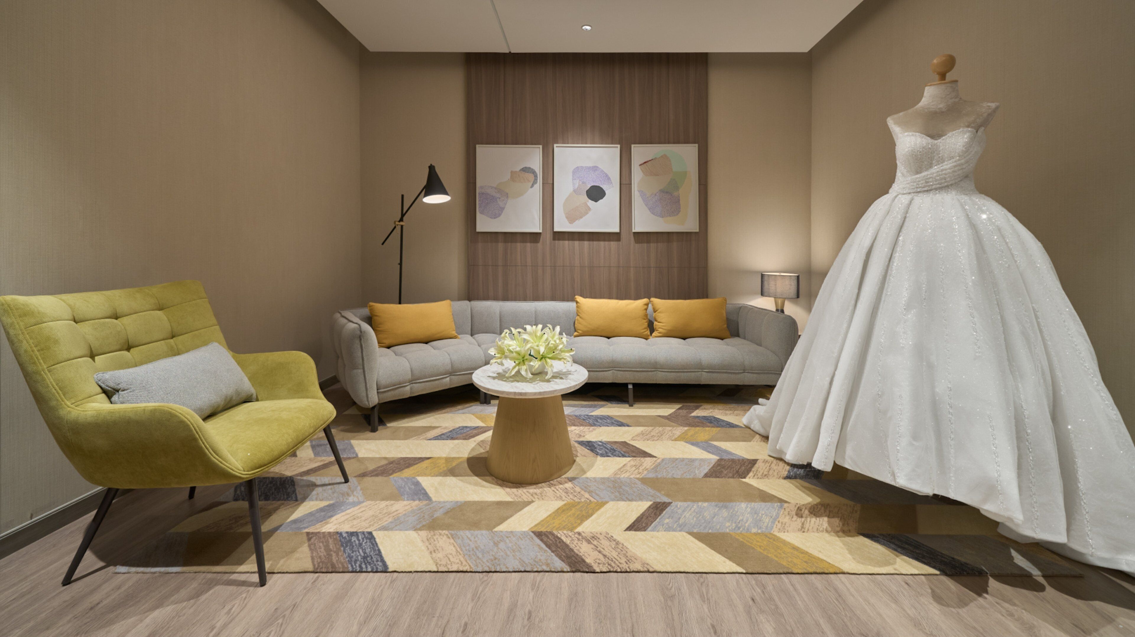 Ein modernes Zimmer mit einem gelben Sessel, einem grauen Sofa mit gelben Kissen, einem weißen Kleid an einer Schönheitsmaske und einem gemusterten Teppich.
