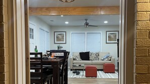 A dining area with a wooden table and chairs, a sofa, and a red ottoman. There is a ceiling fan and recessed lighting. - Gorgeously remodeled Seaside Oasis in Atlantic Beach! (Atlantic Beach)