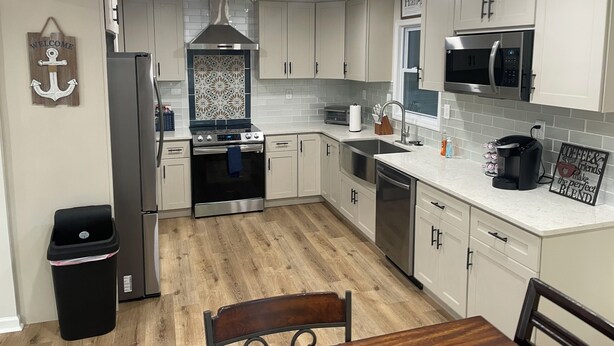A modern kitchen with white cabinets, stainless steel appliances, and a wooden floor. - Gorgeously remodeled Seaside Oasis in Atlantic Beach! (Atlantic Beach)