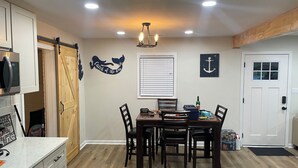 A dining area with a wooden table and chairs, a chandelier, and a wall-mounted anchor decoration. - Gorgeously remodeled Seaside Oasis in Atlantic Beach! (Atlantic Beach)